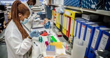 Two young African women putting samples into test tubes in a laboratory