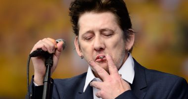 Shane MacGowan smokes a cigarette while performing on stage.