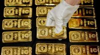A gloved hand arranges one-kilogram gold bars