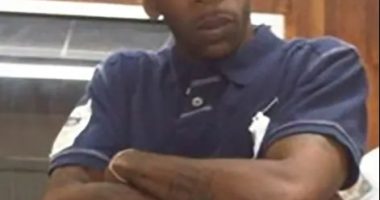 Man wearing a New York Yankees baseball cap and a navy polo shirt with red and white stripes.