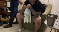 Man seated in a hotel room, holding a towel and looking down at his hands.