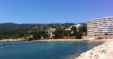 Portals Nous, Majorca: a beach with turquoise water, boats, and buildings on a hillside.