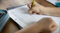 Over the shoulder view of child (8-9) using a pencil to practice handwriting the letters of the alphabet in cursive script