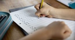 Over the shoulder view of child (8-9) using a pencil to practice handwriting the letters of the alphabet in cursive script