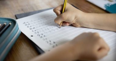 Over the shoulder view of child (8-9) using a pencil to practice handwriting the letters of the alphabet in cursive script
