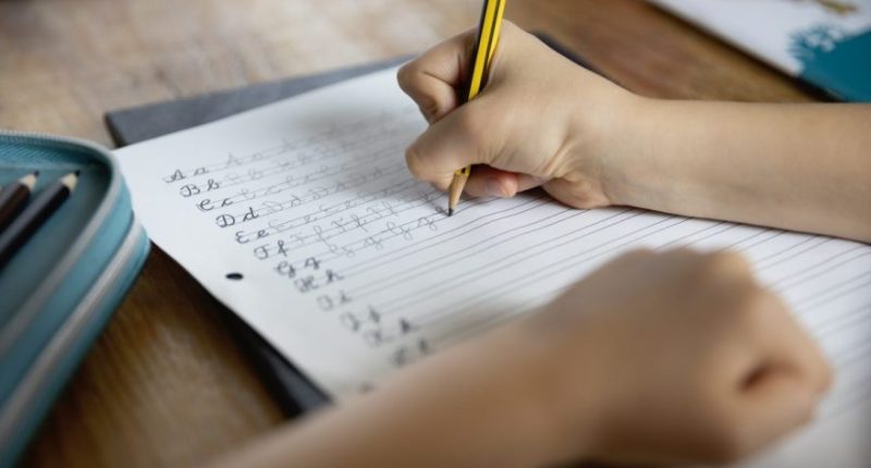 Over the shoulder view of child (8-9) using a pencil to practice handwriting the letters of the alphabet in cursive script