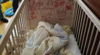 A crib with children's drawings on the headboard and bedding inside.