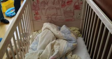 A crib with children's drawings on the headboard and bedding inside.