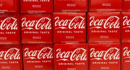 Close-up photo of multiple Coca-Cola 12-packs on a store shelf.