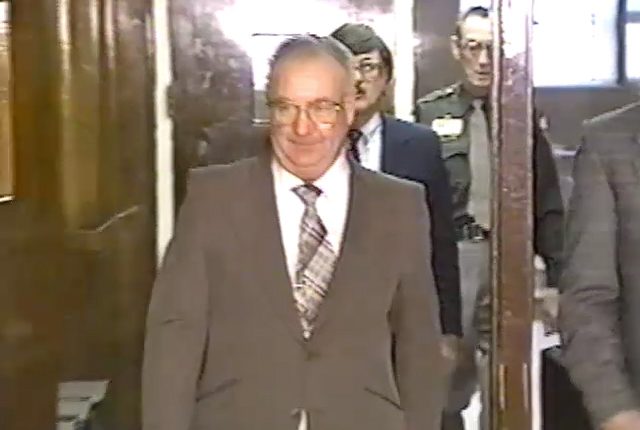 A man in a suit walks down a hallway.