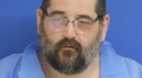 Mugshot of a man with glasses and a beard.