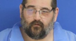 Mugshot of a man with glasses and a beard.