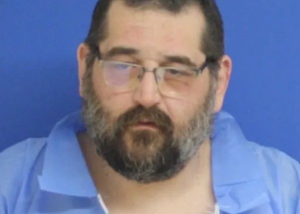 Mugshot of a man with glasses and a beard.