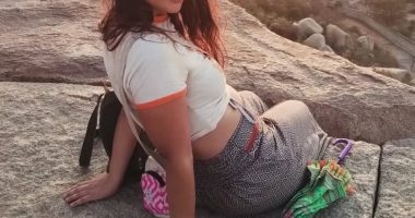 Woman sitting on a rock with an umbrella.