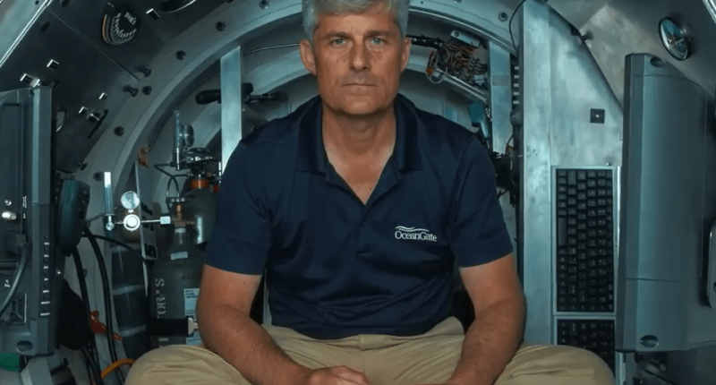Man in OceanGate shirt sitting in a submersible, holding a controller.