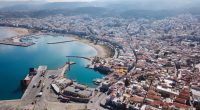 Aerial view of Heraklion, Crete, showing the city's harbor, coastline, and surrounding buildings.