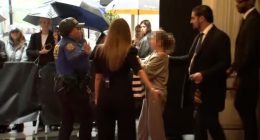 A police officer and security guard escorting a woman through a crowd.