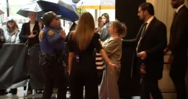 A police officer and security guard escorting a woman through a crowd.