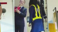 Man in suit exiting airplane, attended by uniformed personnel.