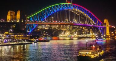 A ferry passes the Sydney Harbour Bridge, lit up in colourful lights as part of the Vivid Sydney festival.