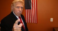 A Donald Trump doppelgänger points at the viewer in front of an American flag.