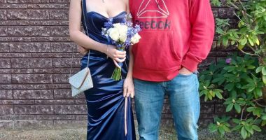 A father and daughter posing for a photo.  The daughter is wearing a dark blue dress and carrying a bouquet.