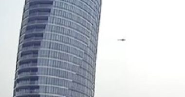 Helicopter flying near a skyscraper.