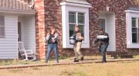 Investigators removing bags and a bucket from a house.