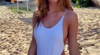 Model Haley Kalil on a beach wearing a white one-piece swimsuit.