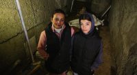 Two women standing in a dark, damaged basement.