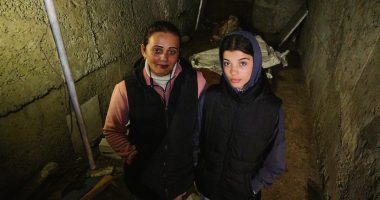 Two women standing in a dark, damaged basement.