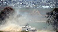 Israeli tank leaving the Gaza Strip, with damaged buildings in the background.