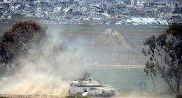 Israeli tank leaving the Gaza Strip, with damaged buildings in the background.