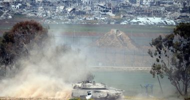 Israeli tank leaving the Gaza Strip, with damaged buildings in the background.