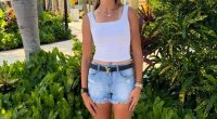 Woman wearing a Miami hat, white tank top, denim shorts, and sneakers.