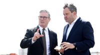 Two men in suits discussing something, one pointing.
