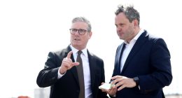 Two men in suits discussing something, one pointing.