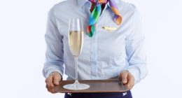 Flight attendant holding a tray with a glass of champagne.