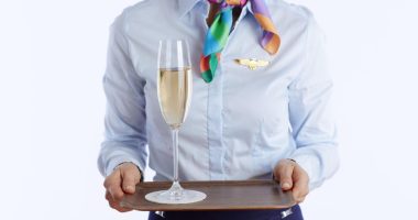 Flight attendant holding a tray with a glass of champagne.