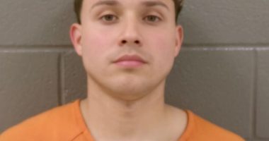 Mugshot of a young man in an orange shirt.