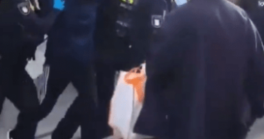 Police officers arresting a hooded person.