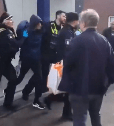 Police officers arresting a hooded person.