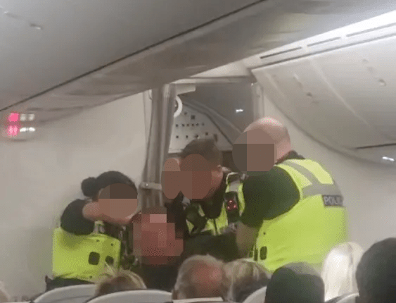 Police officers arresting a disruptive passenger on an airplane.