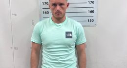 Mugshot of a man in a mint green shirt and black shorts.