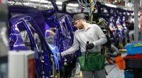 A worker in protective gear adjusts a purple Nissan Juke on the production line at Nissan