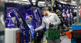 A worker in protective gear adjusts a purple Nissan Juke on the production line at Nissan