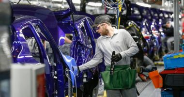 A worker in protective gear adjusts a purple Nissan Juke on the production line at Nissan