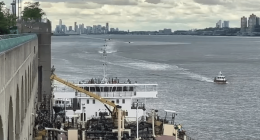 A barge on a river with a city skyline in the background.