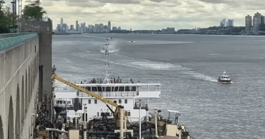 A barge on a river with a city skyline in the background.