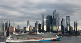 A shot of a cruise ship along the Hudson River in front of Hudson Yards and the Empire State Building in New York